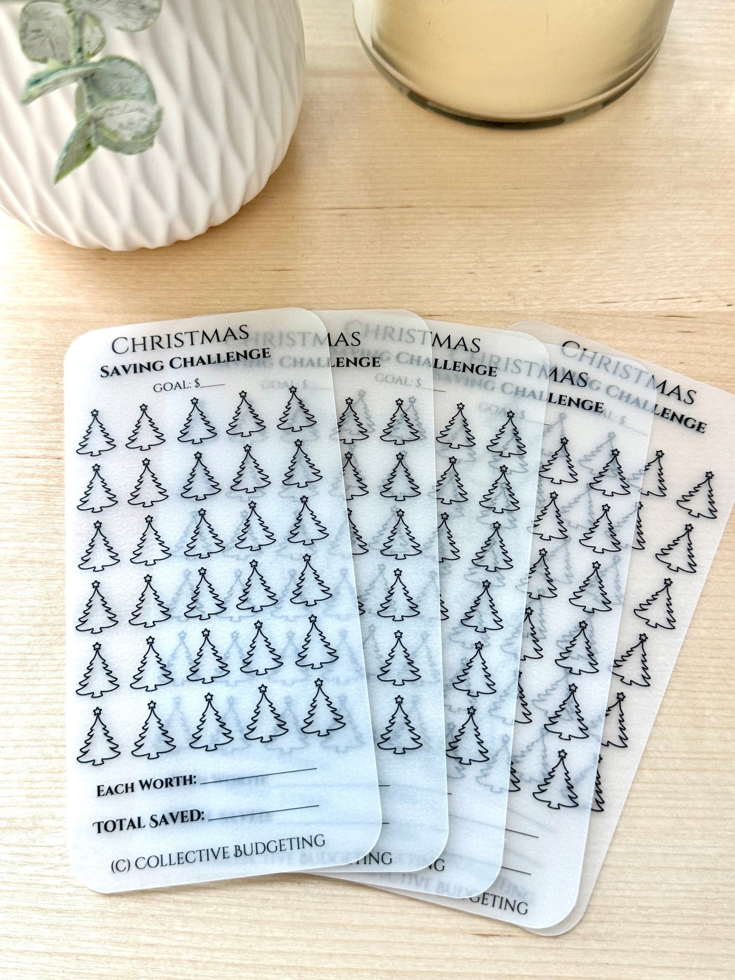 Five transparent sheets with a Christmas saving challenge theme. Each sheet has a goal section, a section with 48 small Christmas tree icons, and a section for writing the amount each icon is worth and the total saved. The text on the sheets reads 'Christmas Saving Challenge', 'Goal: $', 'Each Worth:', 'Total Saved:', and '(C) Collective Budgeting'.
