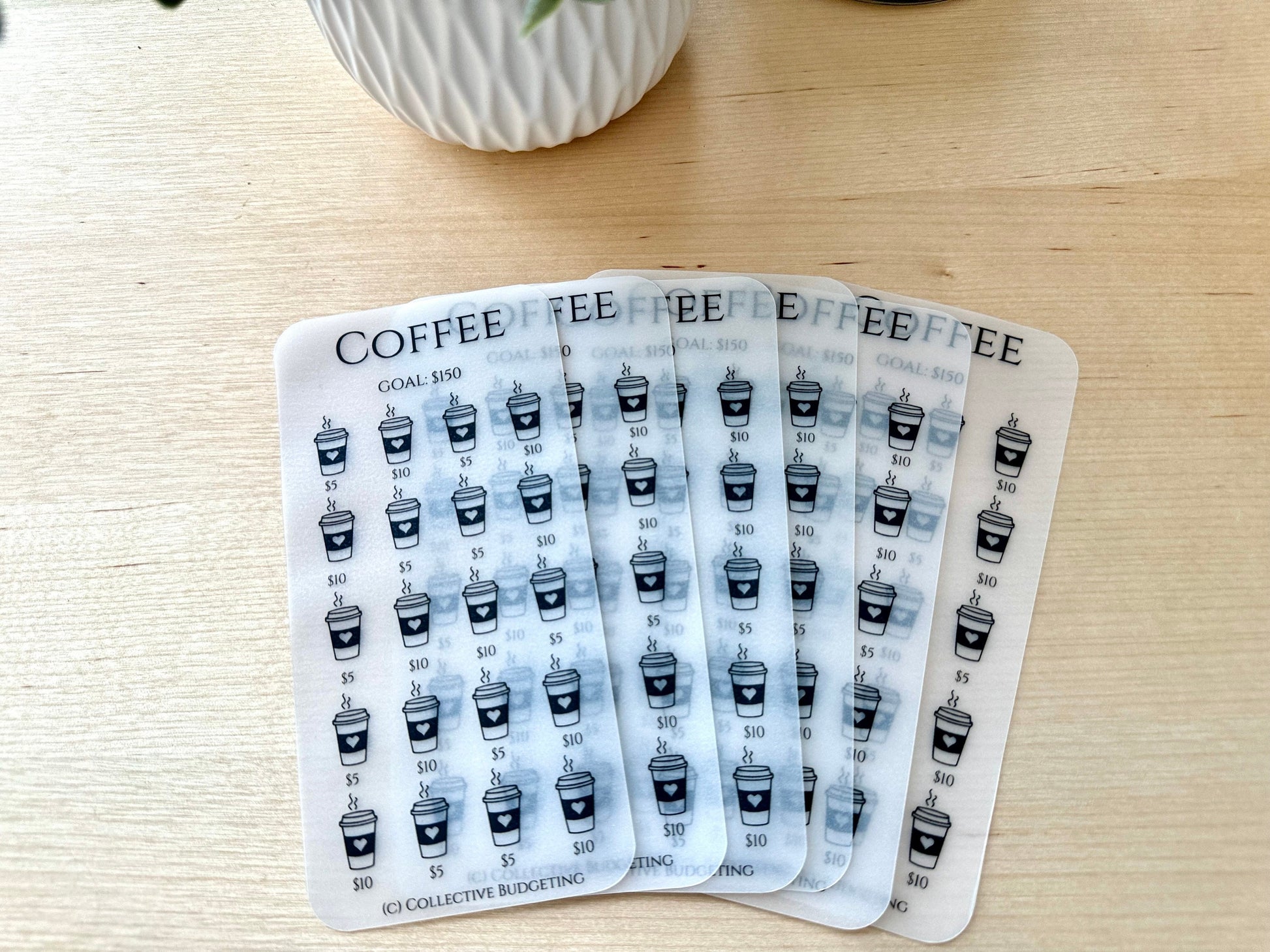 Six transparent sheets with a coffee cup design and the text 'COFFEE' and 'GOAL: $150' printed on them. Each sheet has a grid of coffee cups with the text '$5' and '$10' printed below each cup. The bottom of the sheet has the text '(C) COLLECTIVE BUDGETING'.