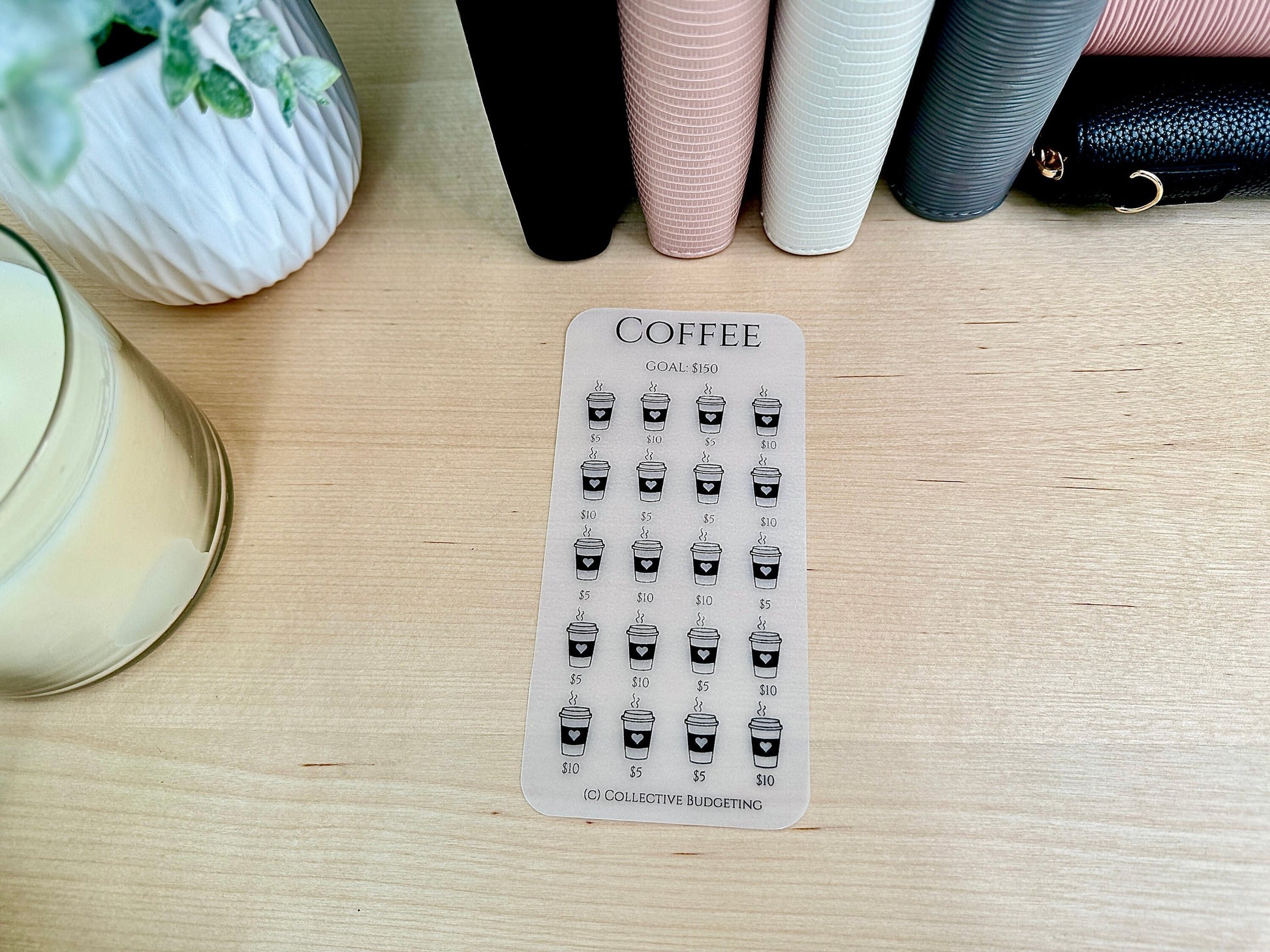 A clear sticker sheet with a coffee cup design. The sticker sheet has the text 'COFFEE' and 'GOAL $150'. The sticker sheet has 25 coffee cup stickers with the text '$5', '$10', and '$15' on each sticker. The sticker sheet has the text '(C) COLLECTIVE BUDGETING' at the bottom.