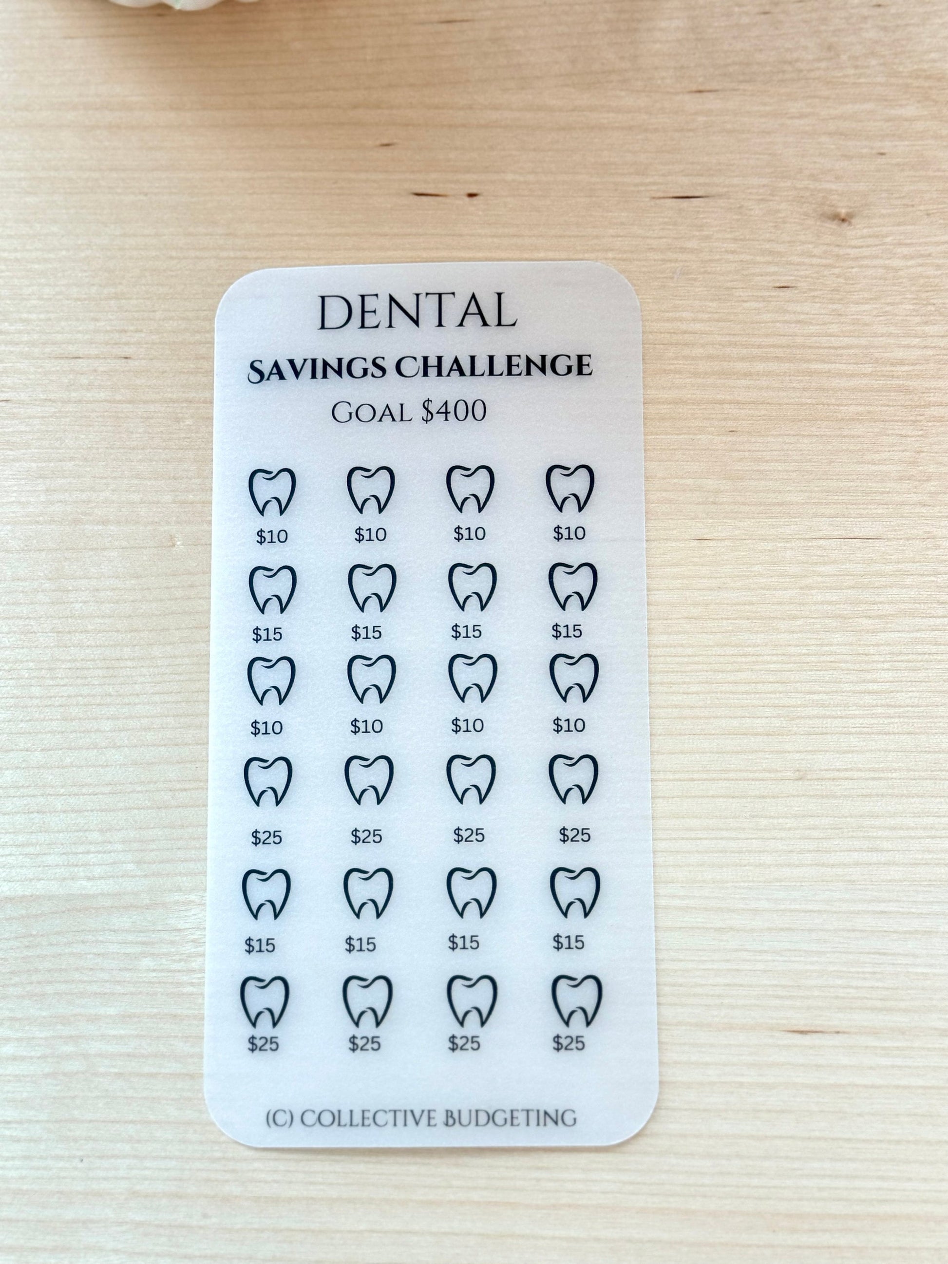 A white card with black text and a black tooth outline. The text reads 'DENTAL SAVINGS CHALLENGE GOAL $400'. There are 24 tooth outlines with dollar amounts underneath each tooth. The dollar amounts are $10, $15, $25. The bottom of the card reads '(C) COLLECTIVE BUDGETING'.