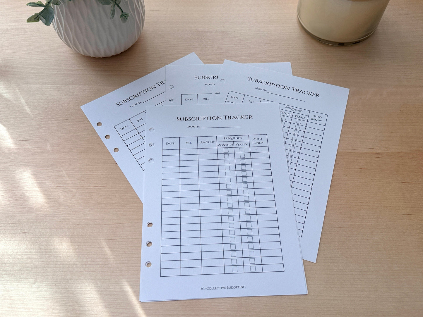 Three white sheets of paper with black text and lines. The sheets are titled 'Subscription Tracker' and have columns for date, bill, amount, frequency, auto renew, and notes. The sheets are on a light brown wooden surface.