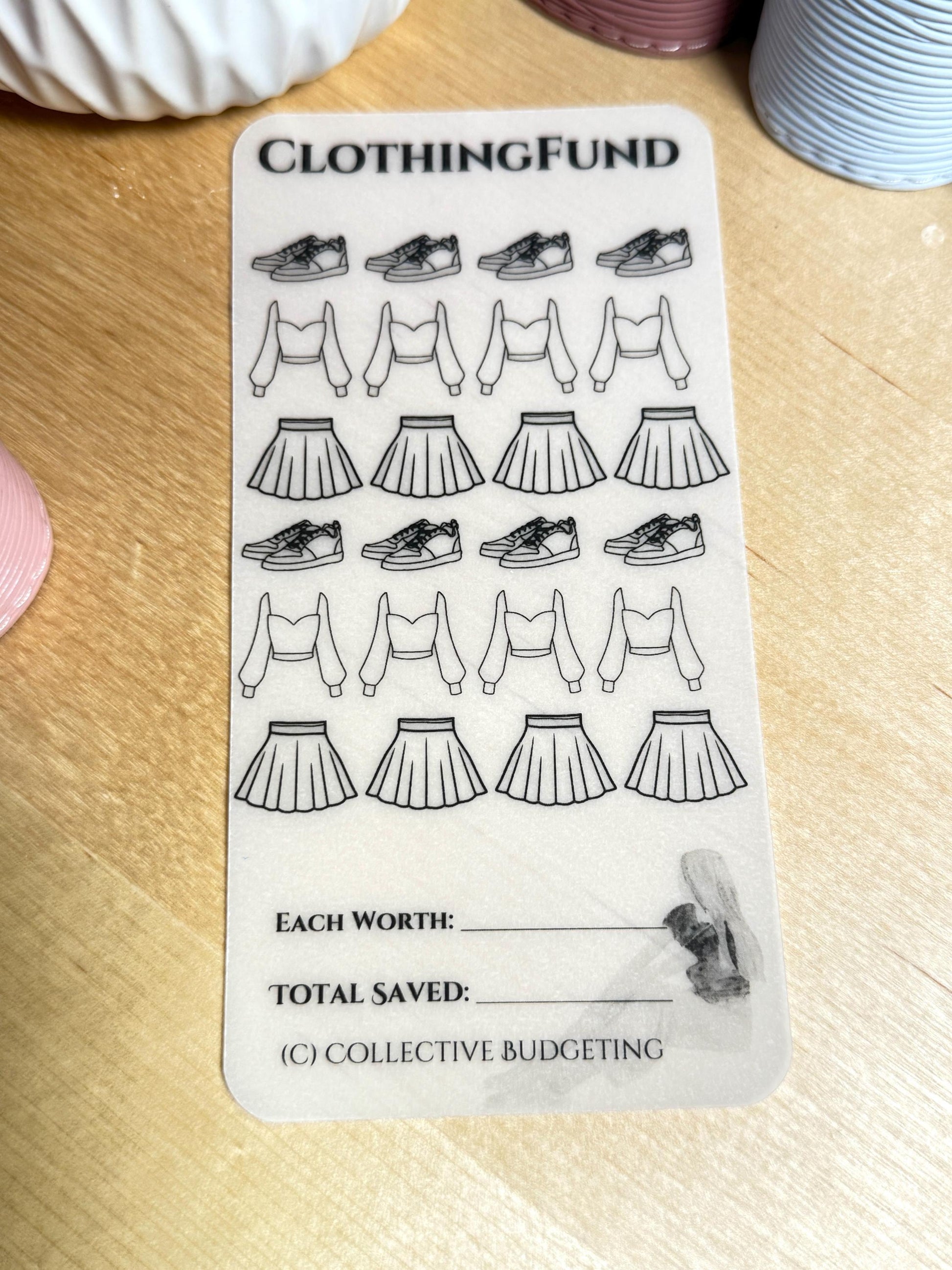 A white sticker sheet with the text 'CLOTHING FUND' at the top. The sheet has 12 black and white drawings of shoes, 12 black and white drawings of crop tops, and 12 black and white drawings of skirts. The sheet also has the text 'EACH WORTH:', 'TOTAL SAVED:', and '(C) COLLECTIVE BUDGETING'.