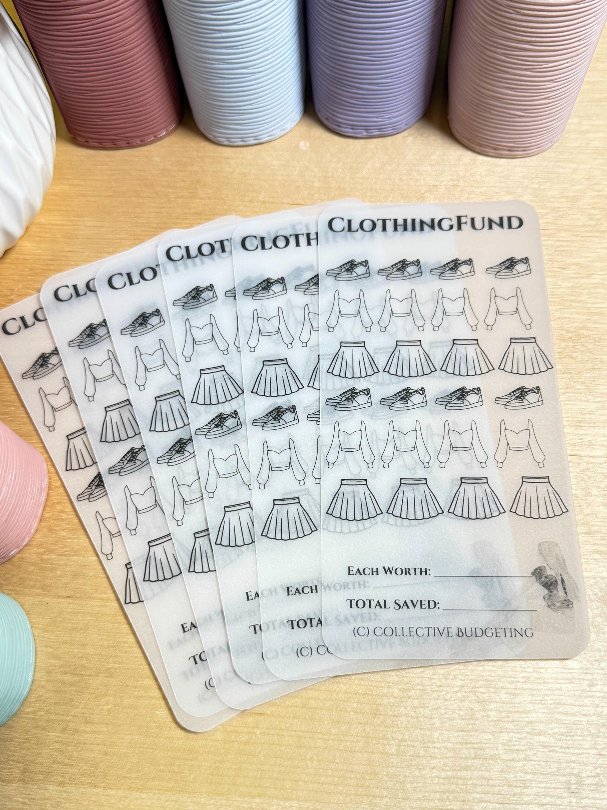 A set of six clear plastic sheets with black outlines of clothing items and shoes. The sheets are labeled 'Clothing Fund' and have a section for 'Each Worth' and 'Total Saved.' The text '(C) Collective Budgeting' is at the bottom of the sheets.
