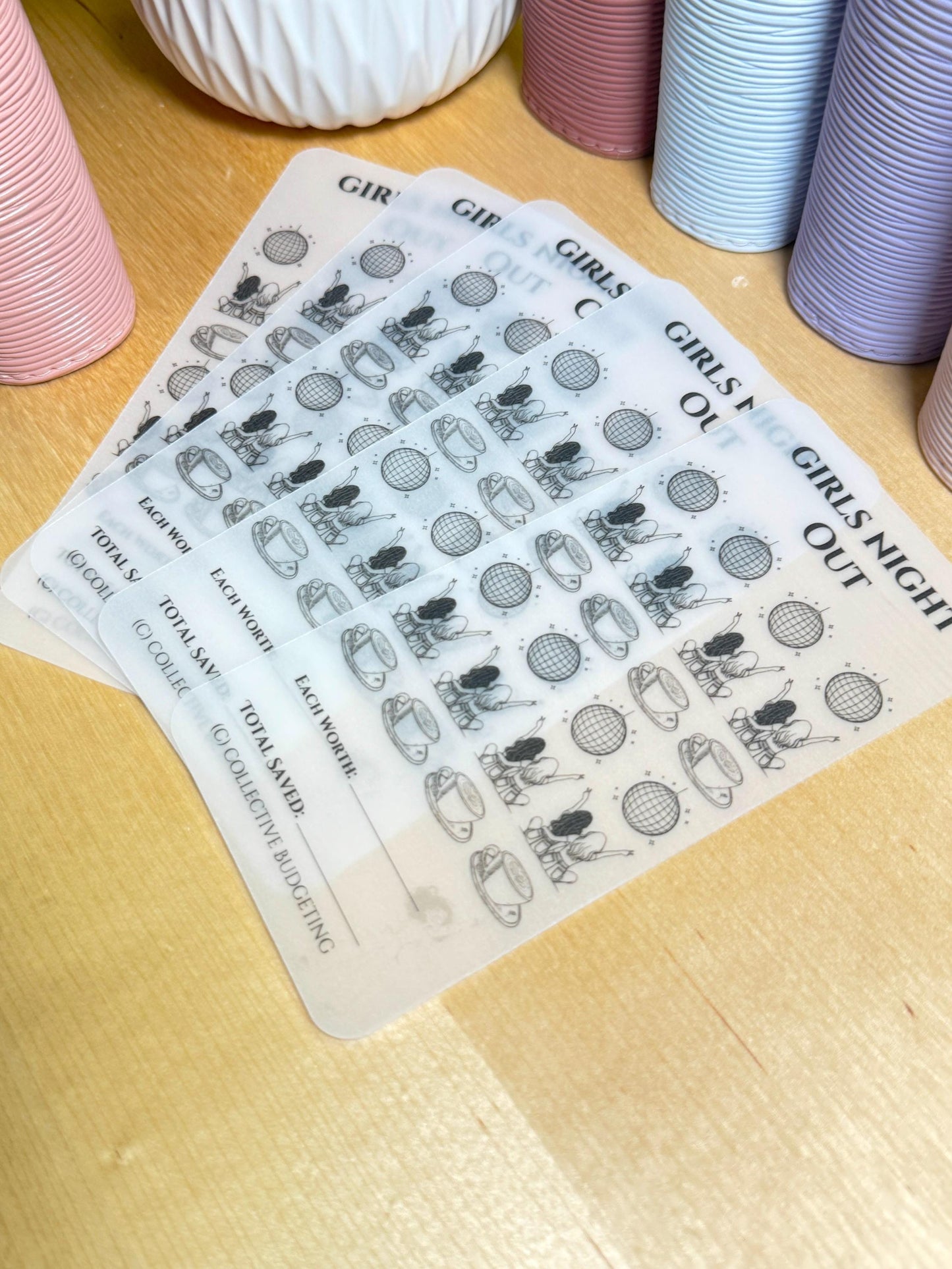Four clear plastic sheets with black ink printed on them. The sheets are stacked on top of each other. The top sheet has the text 'Girls Night Out' printed on it. The other sheets have the text 'Girls Night Out' printed on them. The sheets also have the text 'Each Worth', 'Total Saved', and '(C) Collective Budgeting' printed on them. The sheets have a design of two girls sitting on a couch with a disco ball in the background. The sheets are designed to be