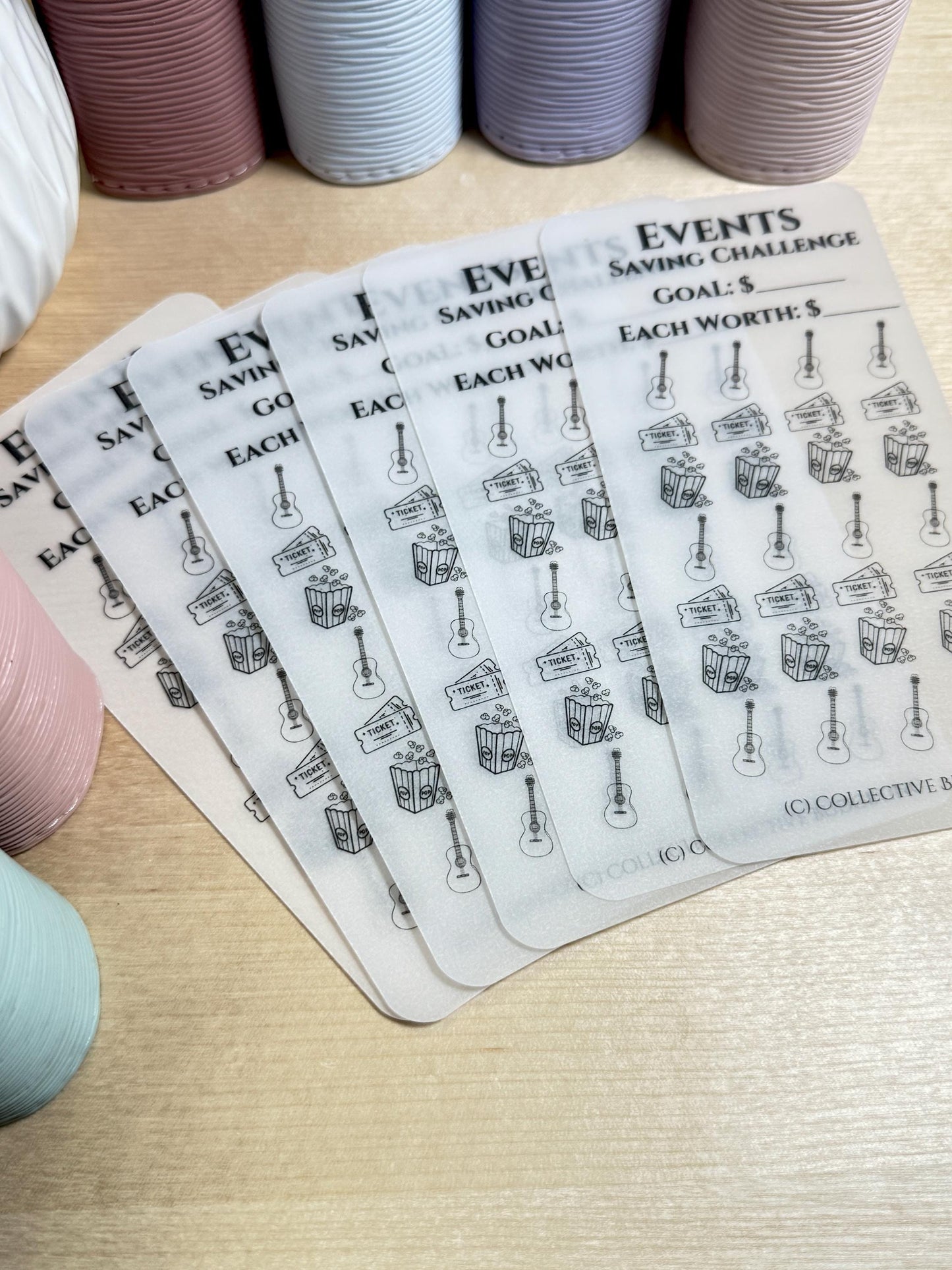 Five transparent sheets with black text and icons. The text reads 'Events Saving Challenge', 'Goal: $', 'Each Worth: $'. The icons are a guitar and a popcorn bucket. The sheets are stacked on top of each other.