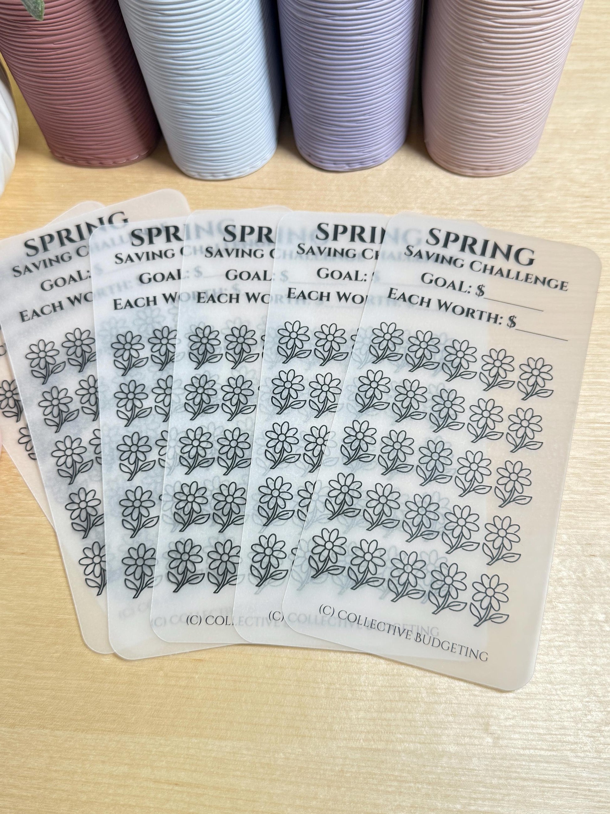 Five transparent sheets with a black and white daisy design. Each sheet has the text 'Spring Saving Challenge' and 'Goal: $' and 'Each Worth: $'. The sheets are stacked on top of each other. The bottom sheet has the text '(C) Collective Budgeting'.