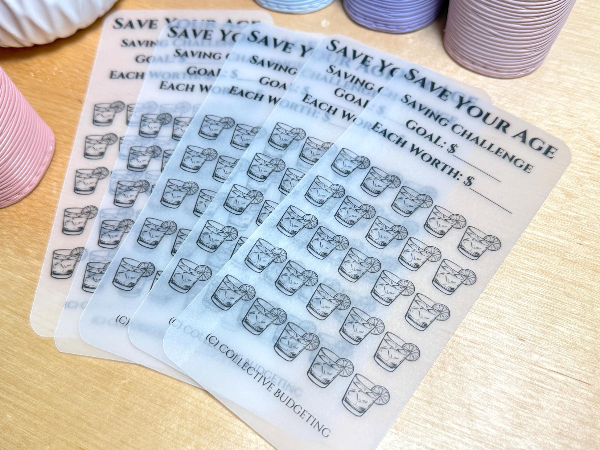 Five transparent sheets with a black and white design of a glass of water with a lime wedge. The sheets have text that reads 'Save Your Age Saving Challenge', 'Goal: $', 'Each Worth: $', '(C) Collective Budgeting'.