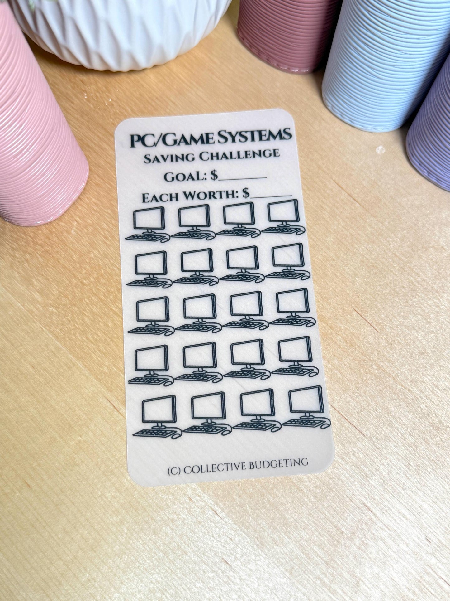 A transparent sticker sheet with a black and white design. The sticker sheet is for a saving challenge. The text on the sticker sheet reads 'PC/GAME SYSTEMS SAVING CHALLENGE GOAL: $ EACH WORTH: $'. The sticker sheet has 25 computer monitor icons with a keyboard and mouse.