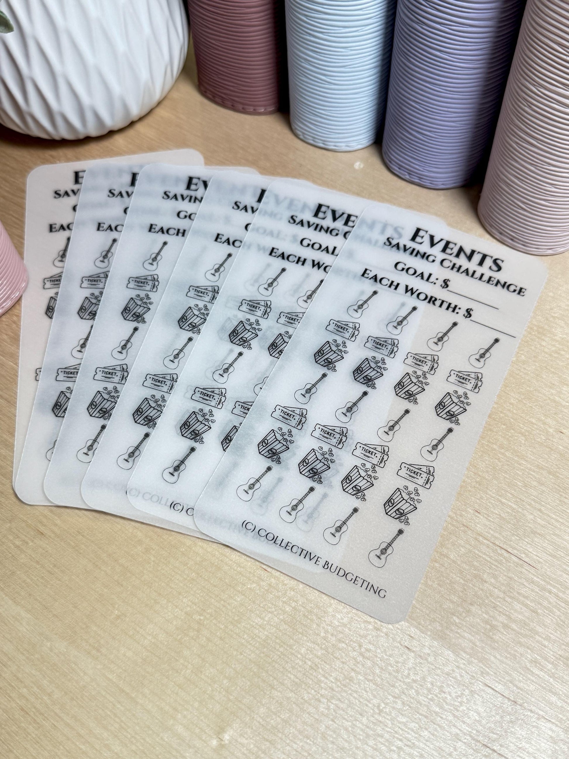 Five transparent sheets with black and white illustrations of a guitar, a box of tickets, and a money bag. The sheets are labeled 'Events Saving Challenge', 'Goal: $', 'Each Worth: $', and '(C) Collective Budgeting'.
