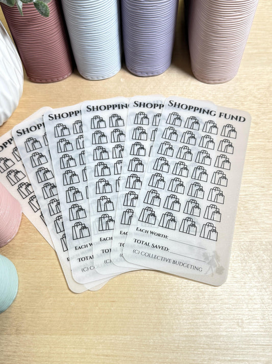 A set of clear, translucent sticker sheets with black shopping bag icons. The sticker sheets are labeled 'Shopping Fund' and have spaces to write 'Each Worth', 'Total Saved', and '(C) Collective Budgeting'.