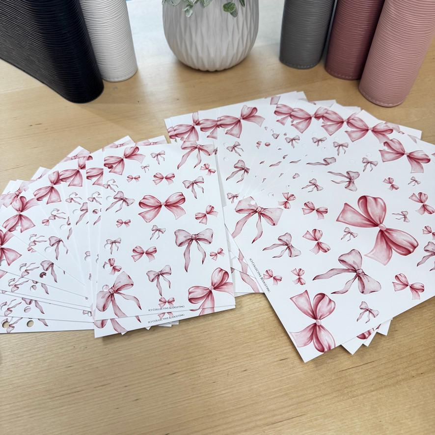A stack of white sheets of paper with pink watercolor bow designs printed on them. The sheets are stacked in a pile with the top sheet showing the most detail. The sheets are all the same size and have a hole punched in the top left corner. The sheets are on a wooden surface.