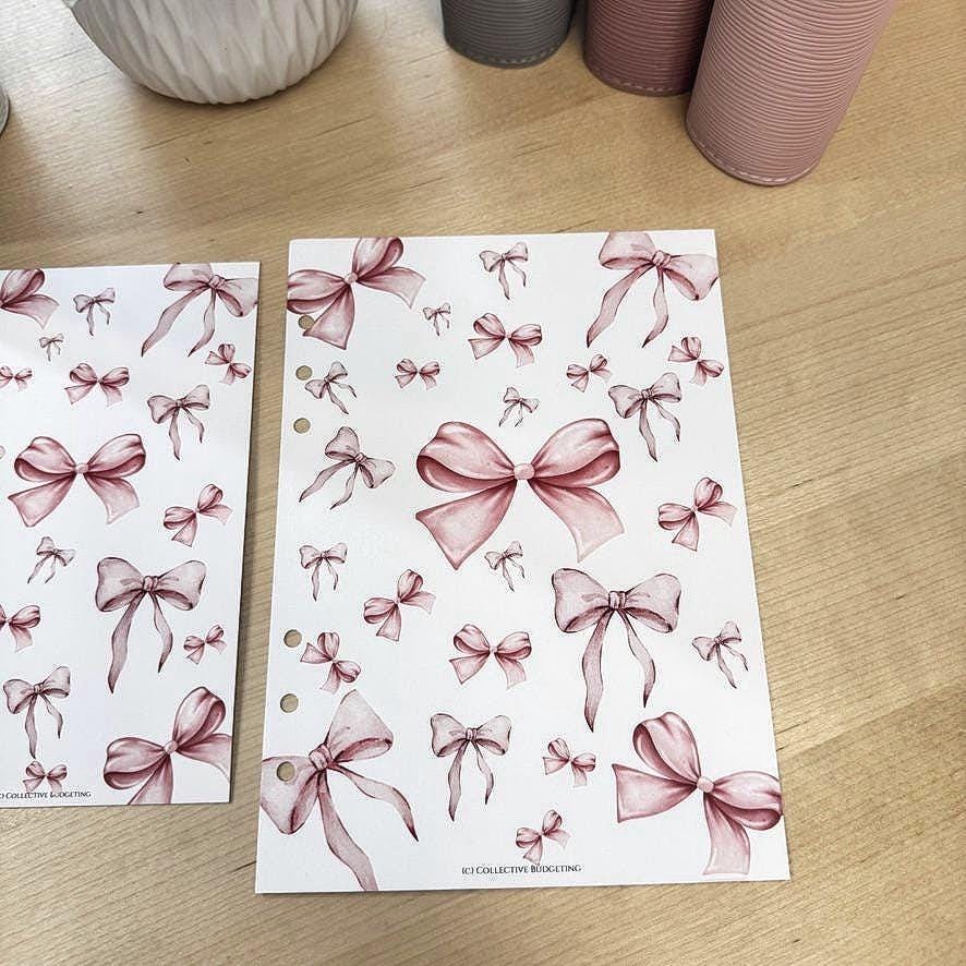 Two sheets of paper with pink watercolor bow designs. The paper is white with pink watercolor bows of various sizes and orientations. The text 'IC3 COLLECTIVE BUDGETING' is printed at the bottom of each sheet.