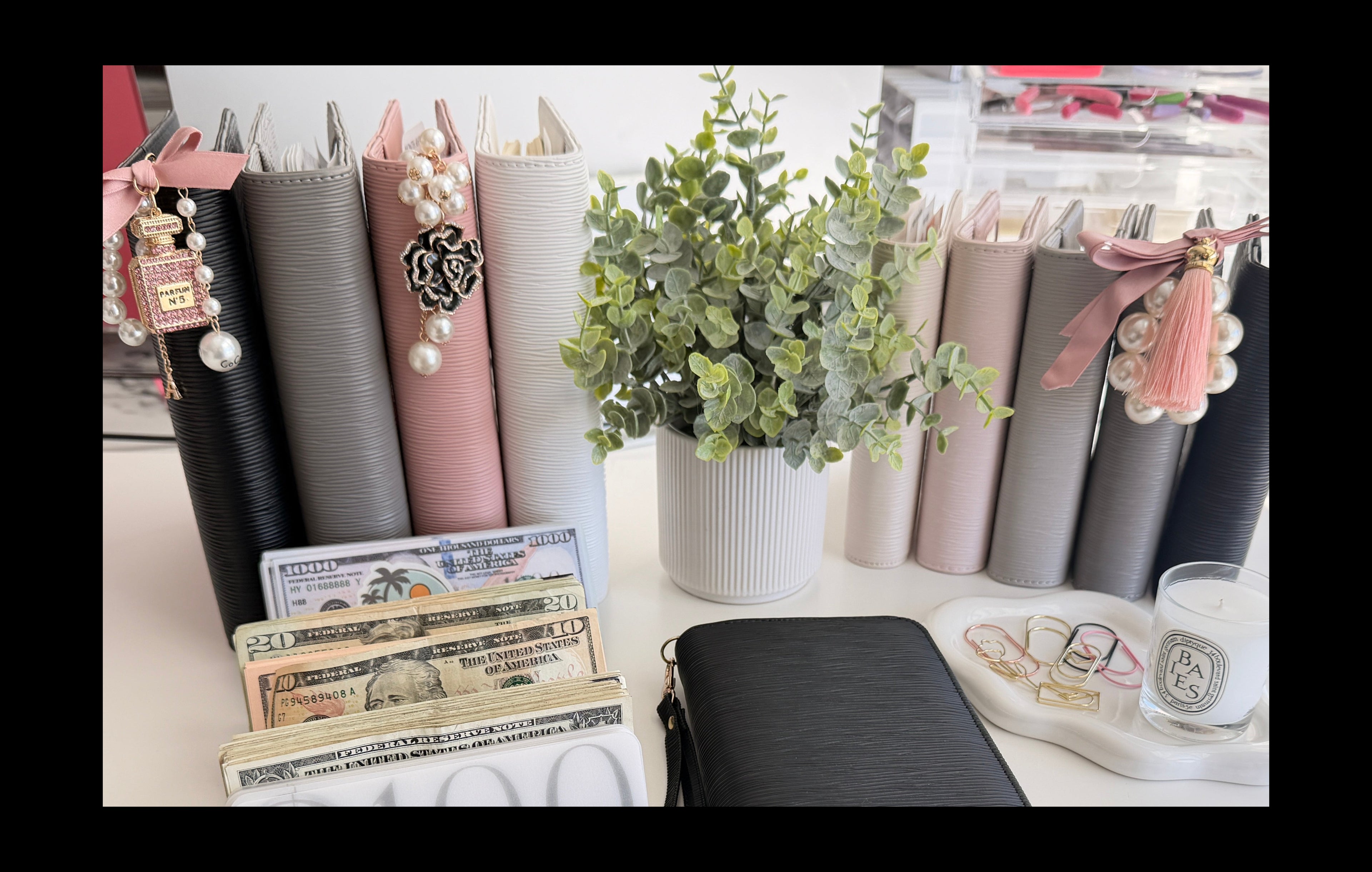 Black wallet, money, and a plant on a desk with stationery items in the background.
